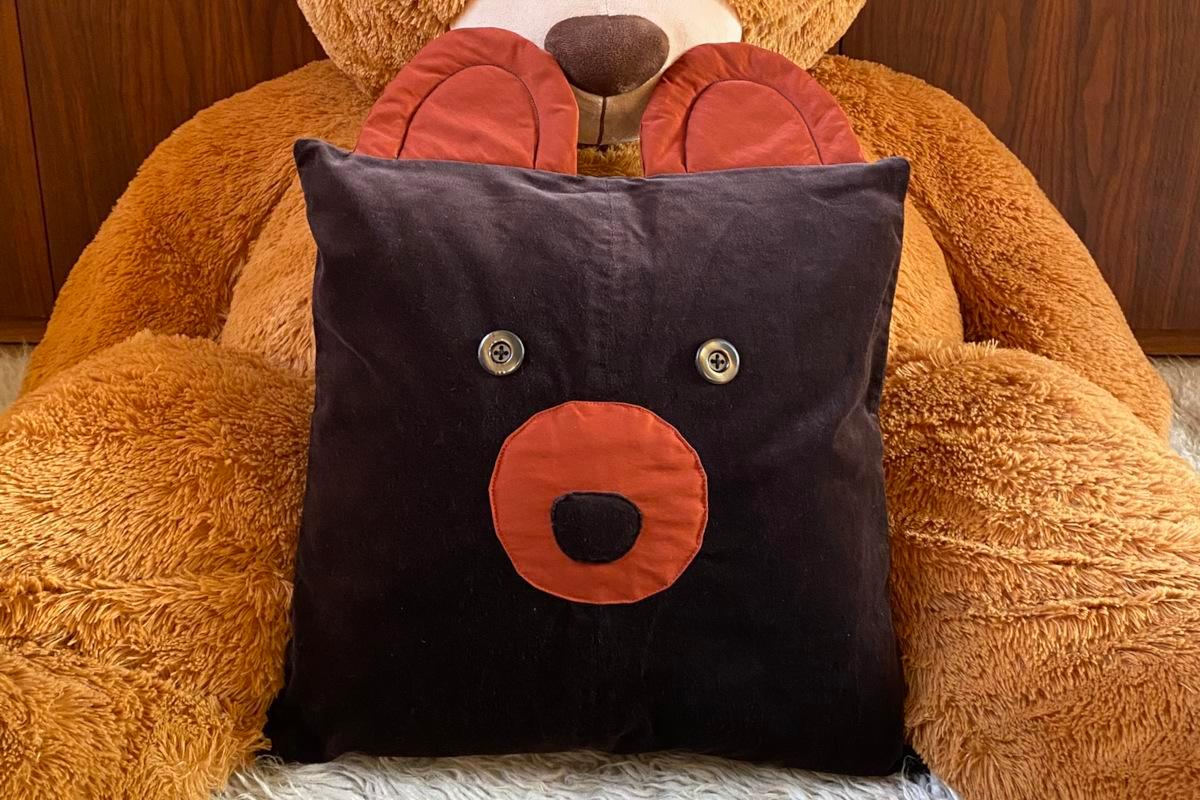 Cuscino artigianale in velluto marrone, con forma di orso e dettagli in rasatello color ruggine.