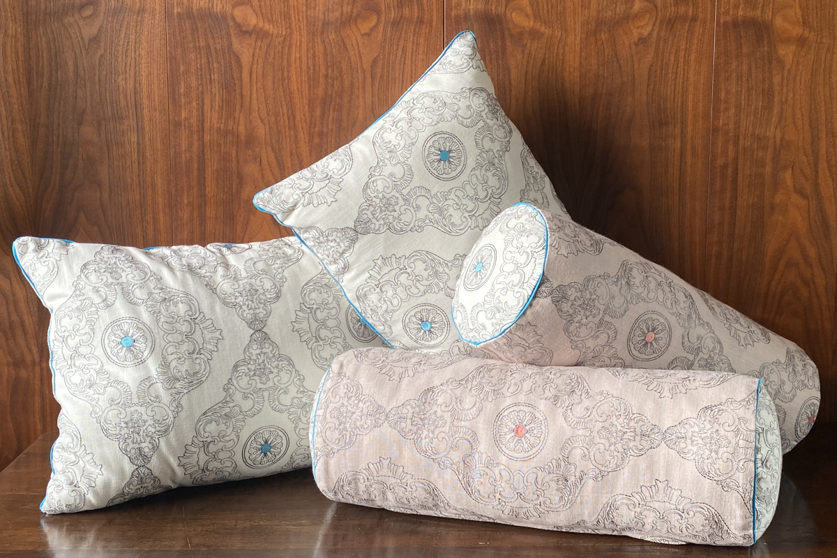 Set di cuscini d'arredo in cotone ricamato nelle eleganti tonalità del bianco, grigio, turchese e rosa pesca.