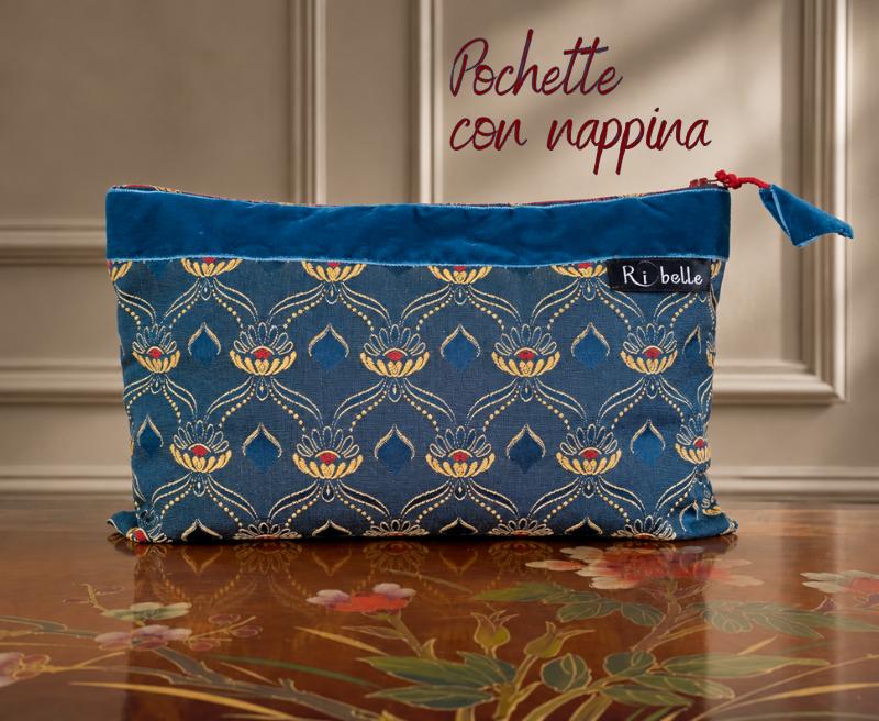 Pochette artigianale in tessuto damascato blu con motivi ornamentali beige dorato e rossi, fascia in velluto blu e nappina coordinata.